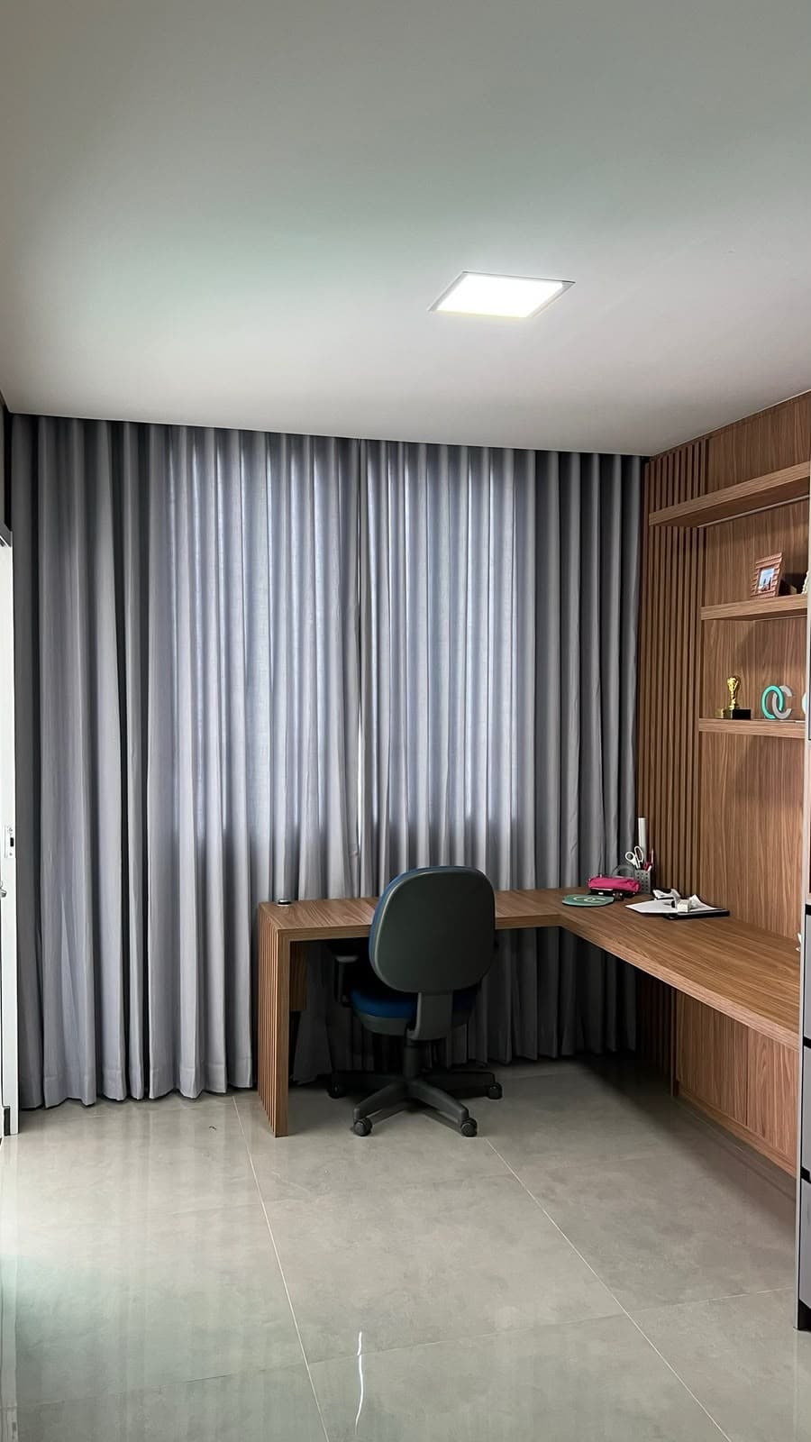 Home office com cortina de linho cinza com forro cobrindo a parede inteira, ao lado de marcenaria ripada