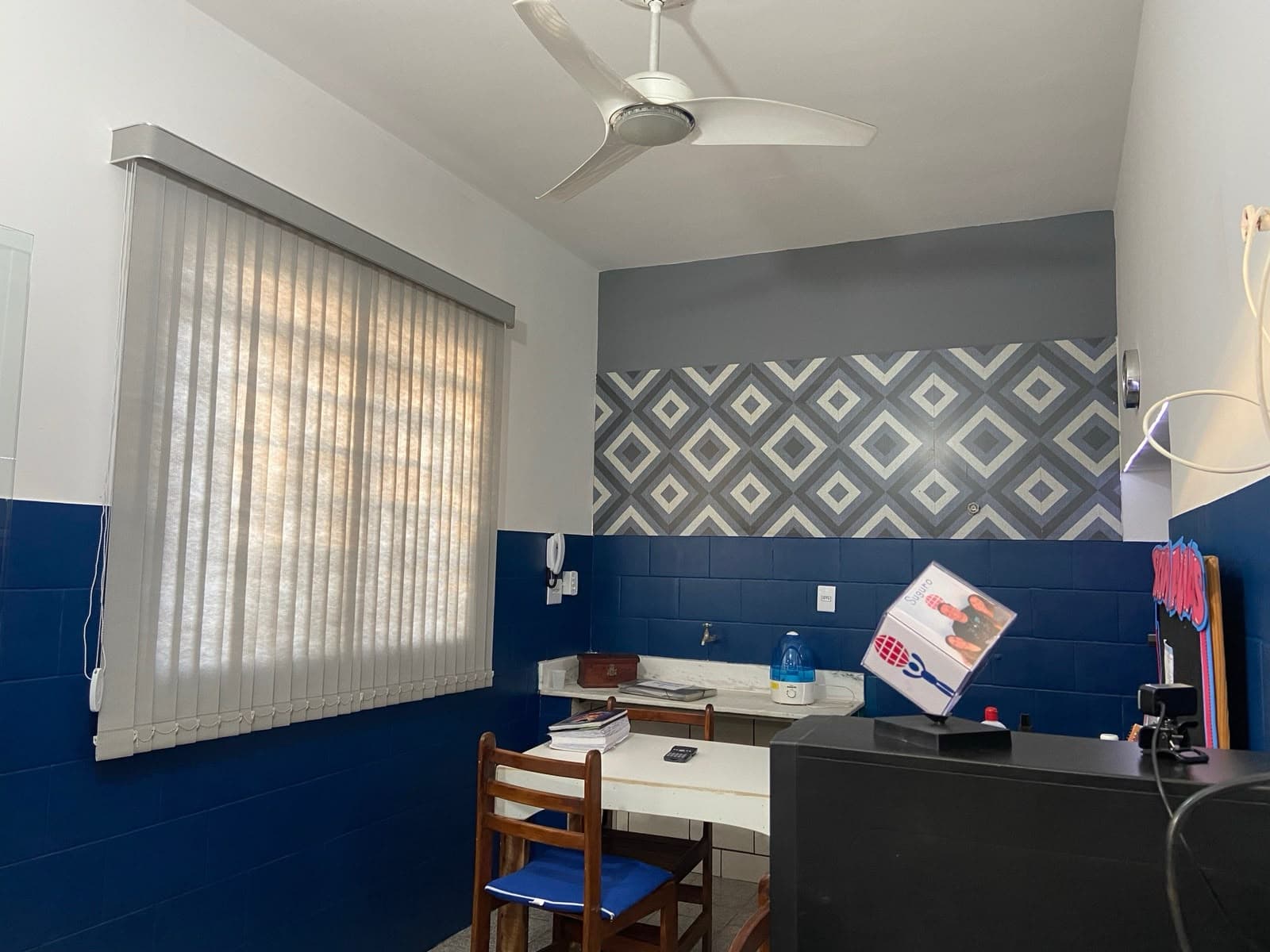 Sala comercial com persiana vertical clara em janela larga, parede azul